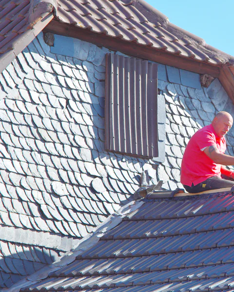A roofer working on a shingled roof